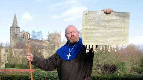 Portrait of priest holding document while standing against church