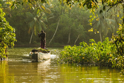 Man standing in boat on river at forest