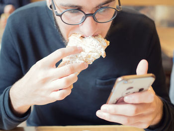 Man eating croissant while using mobile phone