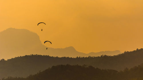 Paragliders flying over mountain range during sunset