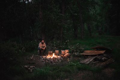 Portrait of mid adult man sitting by campfire in forest