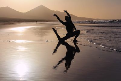 Silhouette man with arms raised on beach against sky during sunset