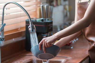 Attractive young woman or housewife washing dishes in the kitchen sink at home.