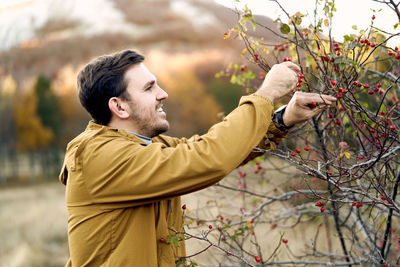 Side view of man with arms outstretched standing against trees