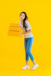 Portrait of smiling young woman standing against yellow background