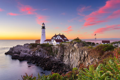 Lighthouse by sea against sky during sunset