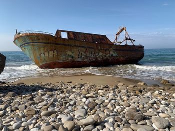 Abandoned ship at beach against sky