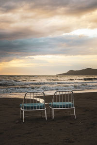 Chairs on beach against sky during sunset