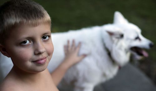 Portrait of shirtless boy with white pomeranian dog at back yard