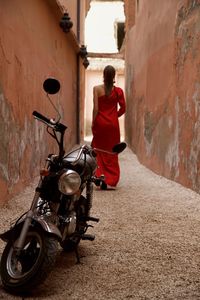 Rear view of man in red cocktail dress leaving her dax motorcycle and walking a reda small street