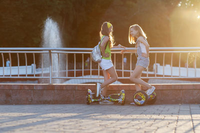 Friends with hoverboards standing by railing against bridge