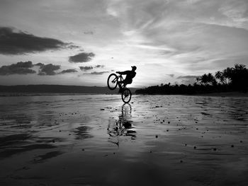 Man riding bicycle by sea against sky