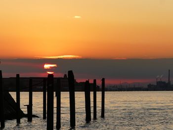 Silhouette wooden posts in sea against sky during sunset