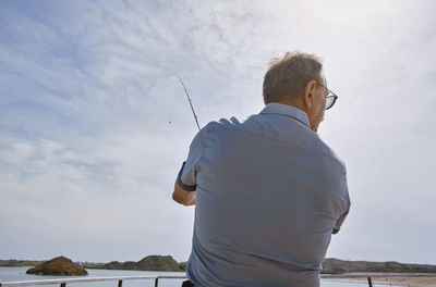 Senior man with fishing rod fishing at jetty