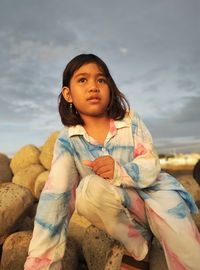 Portrait of girl sitting on rock against sky