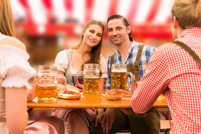 Portrait man and woman with friends having beer at table
