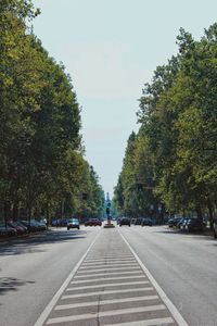 Road amidst trees and city against sky