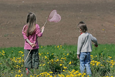 Rear view of siblings with butterfly fishing net while standing on field