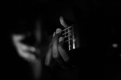 Close-up of hand playing guitar against black background