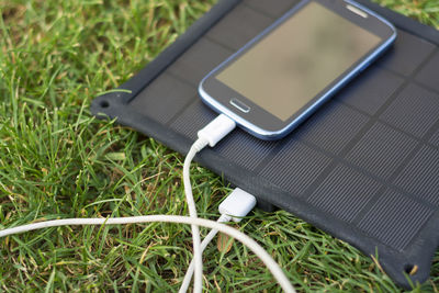 Close-up of mobile phone and solar charger on field