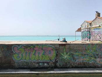 People on wall by sea against clear sky