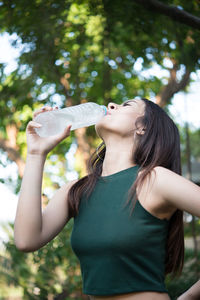 Young woman drinking water while standing outdoors