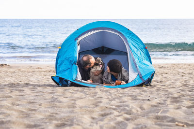 Couple with dog relaxing in tent at beach