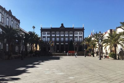 Street amidst trees and buildings against clear blue sky