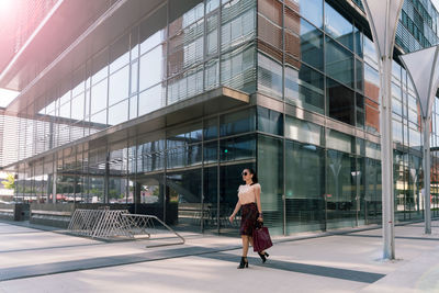 Full length of woman walking by modern building in city