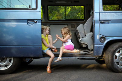 Two girls sitting in doorway of old vintage car holding hands