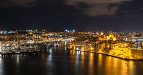 Illuminated buildings by sea against sky at night