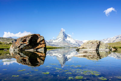 Reflection of rocks in lake against blue sky