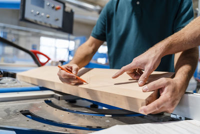 Hands of two carpenters measuring wooden plank