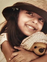 Close-up of smiling girl with hat holding toy while looking away