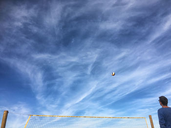 Rear view of man looking at ball over net against sky