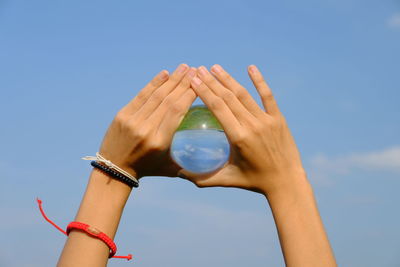 Cropped hands holding crystal ball against blue sky