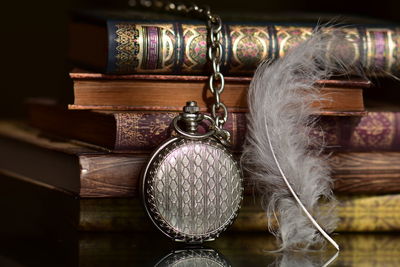 Close-up of pocket watch and feather by stacked books