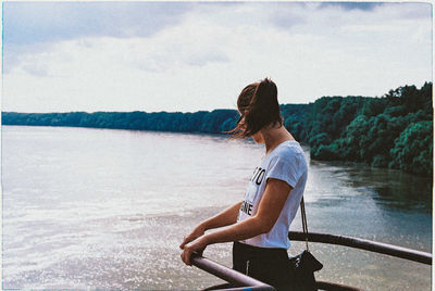 Side view of woman standing by railing while looking at lake against sky