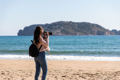 Woman photographing at beach against sky