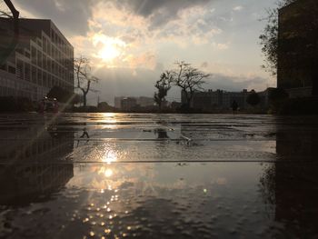 Reflection of silhouette buildings in puddle on street during sunset