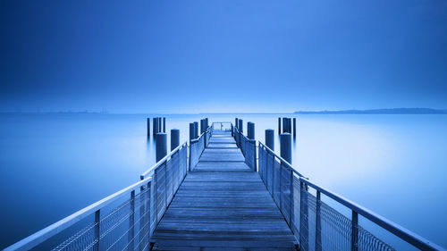 Pier on sea against clear blue sky