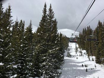 Ski lift over snow covered trees against sky