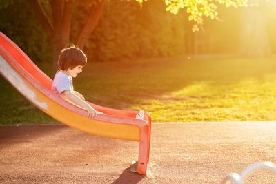 Cute little happy toddler boy playing on slide at playground enjoying sunny summer day