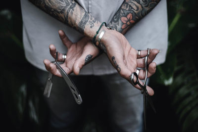 Midsection of man holding scissors and pocket knife while standing by plants