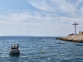 Rocky coastline of saronic gulf, aegean sea, boat and memorial cross at piraeus, attika, greece.