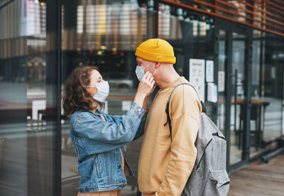 Stylish young family couple hipsters in face mask against glass building, new normal