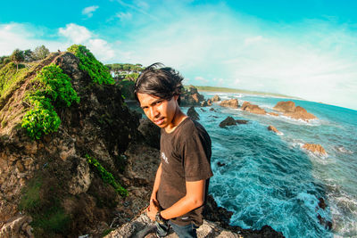 Young woman on rock at beach against sky