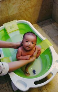 Cropped hands of woman holding cute baby in bathtub