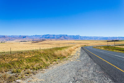 Road amidst field against clear blue sky