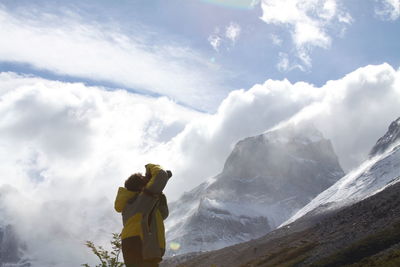 Person photographing mountain against cloudy sky